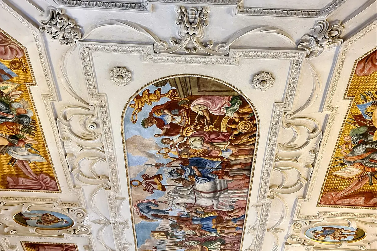 A painted and stuccoed ceiling in the Lobkowicz Palace with a large central fresco framed in white plaster ornament.
