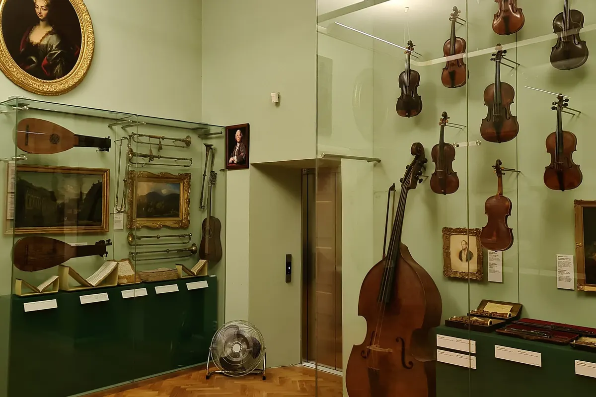 A museum room with lutes, violins and a double bass displayed on the walls and in glass cases.